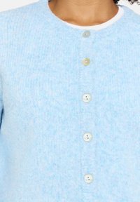 Hellblauer Cardigan aus weicher Wolle mit rundem Ausschnitt und sechs runden, hellen Knöpfen vorne.