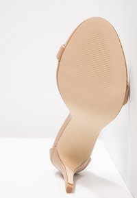 Beiger High-Heel-Schuh von der Sohle gesehen, mit einem schlanken Absatz und subtiler texturierter Griffigkeit im Vorderfußbereich.