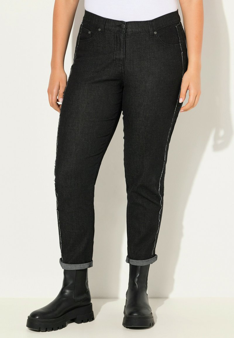 Jeans in denim nero con strisce laterali bianche, taglio aderente, cinque tasche e orli risvoltati, abbinati a robusti stivali neri alla caviglia.