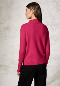 Fuchsia Pullover mit geripptem Kragen und Bündchen, in gerader Passform. Kombiniert mit schwarzen Hosen, von hinten vor einem neutralen Hintergrund gezeigt.