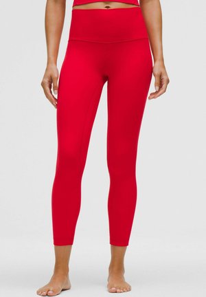 Close-up of a person wearing bright red high-waisted cropped leggings, standing barefoot against a plain background.