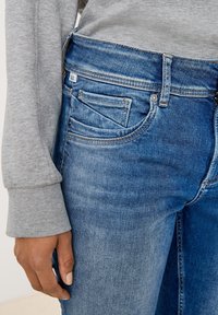 Bledě modré džíny s rovný fit, s pěti kapsami, kontrastním šitím a středním pasem. Viditelný šedý top s dlouhým rukávem.