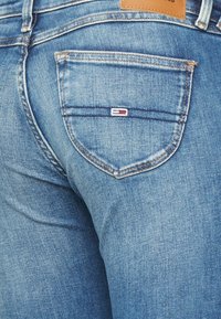 Blå denimjeans med en något urblekt textur, med en signaturlogotyp ovanför den högra bakfickan och stickade detaljer.