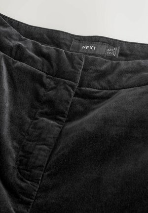 Schwarzer Samtrock mit glatter Textur, ausgestattet mit einem schlichten Bund und sichtbaren Nähdetails. Das Markenetikett "NEXT" ist angebracht.