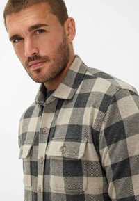 Skjorte i ternet i beige og mørkegrå, lavet af blødt stof. Har to frontlommer, krave og knaplukninger.