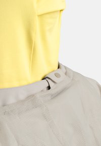 Helles gelbes Kurzarmoberteil, kombiniert mit einem beigen Netzrock mit Druckknopfverschluss und strukturiertem Überlagermuster.