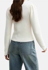 Biały, teksturowany sweter z prążkowanym wzorem i bufkami na ramionach, zestawiony z jasnoniebieskimi, wysokim stanem jeansami z tylnymi kieszeniami.