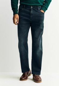 Tumesinised teksapüksid sirge lõikega, ees taskud ja nööpkinnitusega, koos pruunide nahast kingadega.