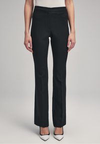 Pantalon noir ajusté avec un design droit, texture lisse, taille mi-haute et détails de couture à l'avant, associé à des chaussures blanches à bout pointu.