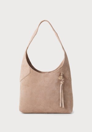 Sac à épaule en daim beige clair, présentant une large ouverture, une forme arrondie, un détail de pompon noué et un accent décoratif en or.