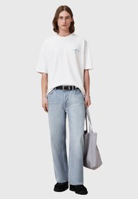 Hvid oversized t-shirt med lys blå logo, parret med lys blå jeans og sorte platform sko, holder en grå tote bag.
