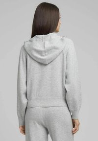 Sudadera gris con capucha hecha de tela suave, con un ajuste relajado, puños acanalados y un bolsillo tipo canguro. Vista trasera que destaca el detalle de la capucha.