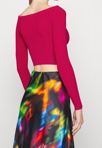 Top ajustado de canalé, sin mangas, en magenta, combinado con una falda de patrón abstracto multicolor, que presenta un diseño recortado y mangas largas.