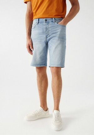 Jasnoniebieskie szorty z denimu o luźnym kroju, z pięcioma kieszeniami i postrzępionym wykończeniem. W połączeniu z gładkim pomarańczowym t-shirtem i białymi trampkami.