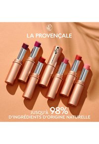 Huit rouges à lèvres dans des tubes en or rose présentent diverses nuances de rose et de rouge. L'emballage est équipé d'un capuchon argenté avec un logo de marque.