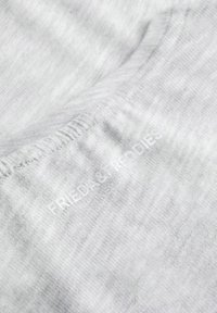 Hellgrauer Stoff, weiche Textur, sichtbare Nähte, mit einem dezenten Aufdruck des Logos "FRIEDA & FREDDIES" nahe dem Rand.