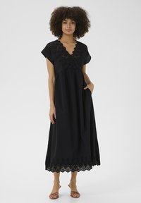 Black dress with short sleeves, V-neck, and intricate eyelet detailing along the bodice and hem, featuring a flowy silhouette and pockets.