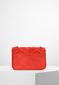 Červený prošívaný batoh s šikmým vzorem, vyrobený z měkkého materiálu. Obsahuje zipové zapínání a jednoduchý obdélníkový tvar.