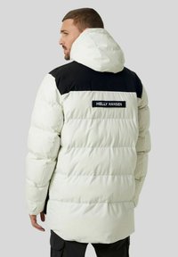 Giubbotto piumino bianco e nero, con cappuccio, cuciture orizzontali e logo Helly Hansen sul retro. Texture liscia e design voluminoso.