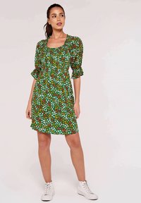 Grünes Blumenkleid mit puffärmeligen Ärmeln und quadratischem Ausschnitt, das mit verstreuten weißen, orangefarbenen und roten Blumenmustern auf grünem Hintergrund verziert ist.