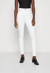 Vaqueros blancos ajustados de talle medio, con diseño de cinco bolsillos y costuras sutiles. Combinados con tacones negros de punta abierta.