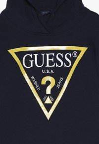 Sudadera azul marina con un gran logotipo de triángulo amarillo que presenta "GUESS® U.S.A. WASHED JEANS" y un diseño de signo de interrogación en el centro.