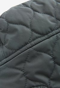 Tissu noir matelassé avec une texture lisse, présentant des motifs de couture arrondis. Le matériau semble léger et flexible.