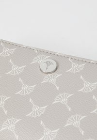 Close-up of a light gray textured wallet with a repeating white geometric pattern and a round metal button embossed with the same design.
