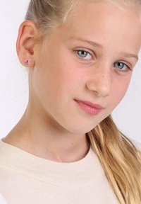 Roze edelsteen studoorbellen op een model met lichtblond haar, dat een crèmekleurige trui draagt. De oorbellen zijn klein en vierkant van vorm.
