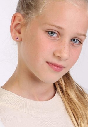 Rosa Schmucksteinstud-Ohrringe an einem Modell mit hellblondem Haar, das einen кремfarbenen Pullover trägt. Die Ohrringe sind klein und quadratisch.