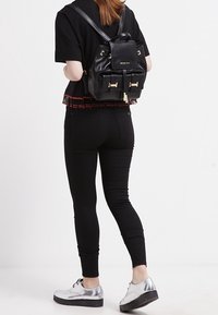 Zaino in pelle nera con dettagli in oro, due tasche frontali e spalline regolabili. Indossato con pantaloni neri attillati e scarpe con plateau argento.