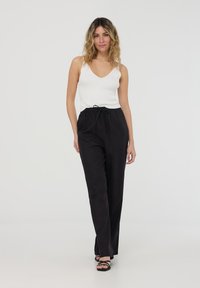 Pantaloni neri larghi con vita elastica e cordoncino, abbinati a un top in cotone bianco a coste. Tessuto morbido con un design informale.