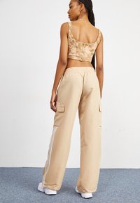 Μπέζ κοντό τοπ με λουλουδάτο μοτίβο, συνδυασμένο με φαρδιά μπέζ cargo παντελόνια που διαθέτουν πλαϊνές τσέπες και λευκές ρίγες κατά μήκος των ποδιών.