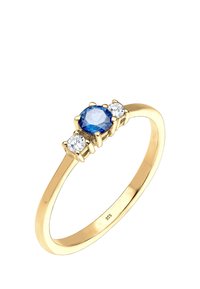 Anillo de oro con una gema azul ovalada central flanqueada por dos piedras redondas transparentes. La banda es elegante y pulida, marcada "925."