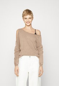 Top marrón de manga larga, con escote off-shoulder y tela texturizada, con un ligero desgaste, usado sobre una camiseta negra de tirantes. Combinado con pantalones blancos de cintura alta.