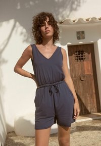 Marineblaues ärmelloses Jumpsuit mit V-Ausschnitt, elastischem Taillenbund und Kordelzug. Weicher Stoff, lockere Passform, geeignet für warmes Wetter.