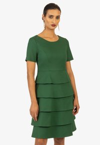 Grünes Kleid aus strukturiertem Stoff, mit kurzen Ärmeln, einem runden Ausschnitt und geschichteten Volants am Saum.