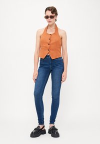 Halter nyakú narancssárga cropped atléta, gombos záródással, sötétkék skinny farmernadrággal és masszív fekete platform cipővel párosítva.