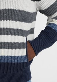Strickpullover mit horizontalen Streifen in Marineblau, Grau und Weiß. Rippbündchen und Saum, mit einem strukturierten Muster für zusätzlichen Detailreichtum.
