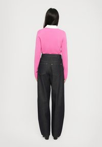 Rosa strikkegenser med hvit krage, kombinert med mørkeblå, vide denimbukser. Har to baklommer og en avslappet passform.