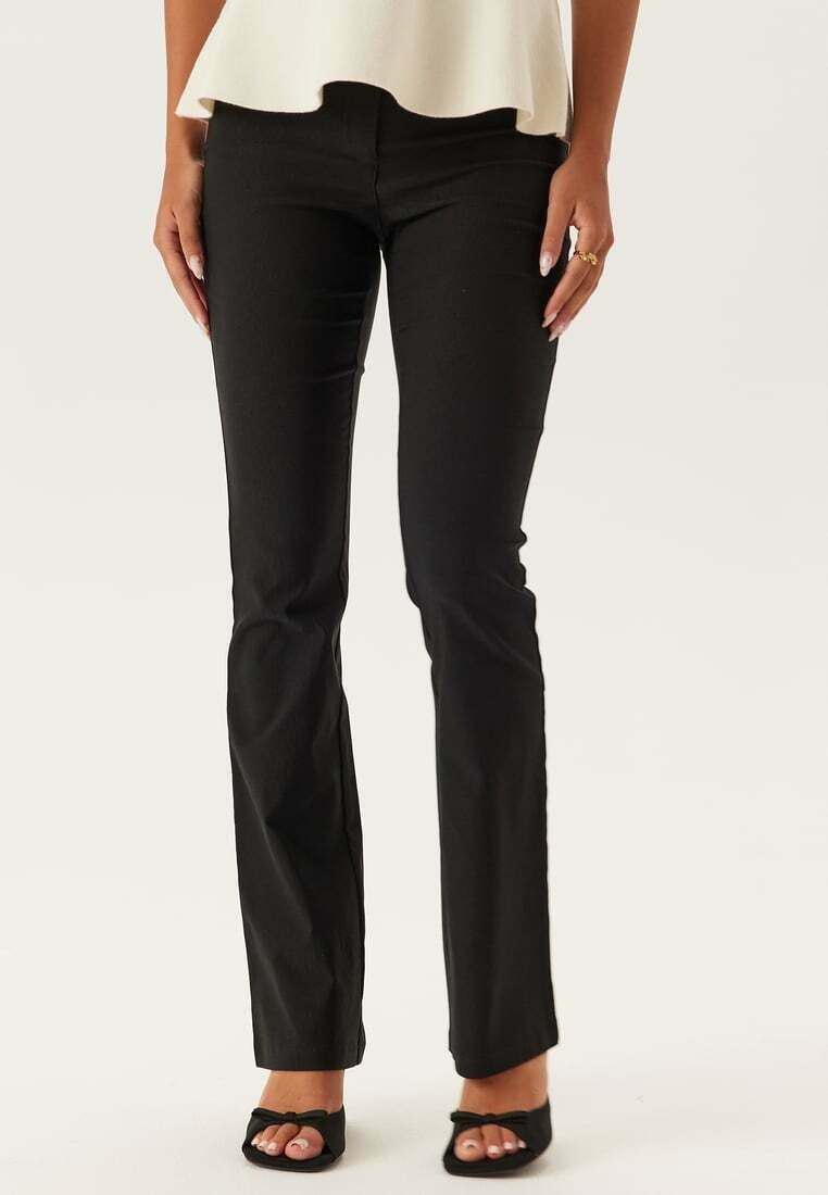 Zwarte, slim-fit broeken met een gladde textuur en een lichte flare bij de enkels, gecombineerd met zwart open schoenen.