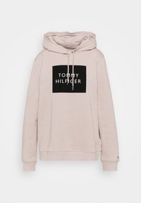 Felpa rosa chiaro con cappuccio, caratterizzata da una grafica quadrata nera con il testo bianco "TOMMY HILFIGER". Cordini al cappuccio e polsini a coste. Tessuto morbido.