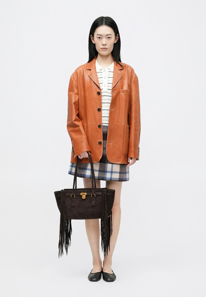 Brun læder oversized jakke, hvid mønstret top, ternet nederdel med blå og beige, sorte flade sko og en mørk ruskinds håndtaske med frynser.