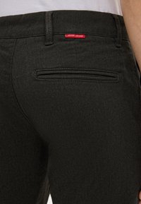 Zbliżenie na ciemne spodnie w wzór w jodełkę z tylną kieszenią i małą etykietą "JOOP! JEANS" w pobliżu pasa.