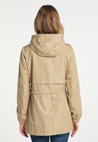 Béžová nepromokavá bunda s kapucí, nastavitelným pasem, elastickými manžetami a hladkou texturou. Má jednoduchý design bez viditelných vzorů.