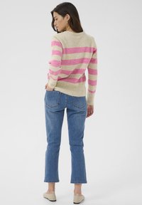 Striped sweater with pink and beige colors, soft texture. Paired with blue jeans and beige slip-on shoes, showing a relaxed fit and casual style.