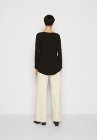 Maglietta nera a maniche lunghe con orlo arrotondato, abbinata a pantaloni larghi color crema. Texture liscia e design semplice, senza motivi visibili o accessori.