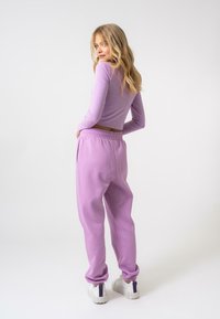 Top a maniche lunghe lilla e pantaloni coordinati, realizzati in tessuto morbido. Presentano una vita elasticizzata e caviglie a costine, abbinati a sneaker bianche.