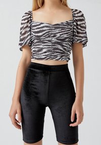 Haut court à imprimé zèbre noir et blanc avec manches bouffantes, associé à un short cycliste noir brillant taille haute. Texture lisse, coupe ajustée.