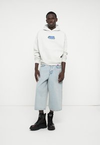 Sudadera gris con diseño gráfico azul, pantalones cortos de mezclilla claros y anchos, y botas negras de tobillo con suela gruesa.